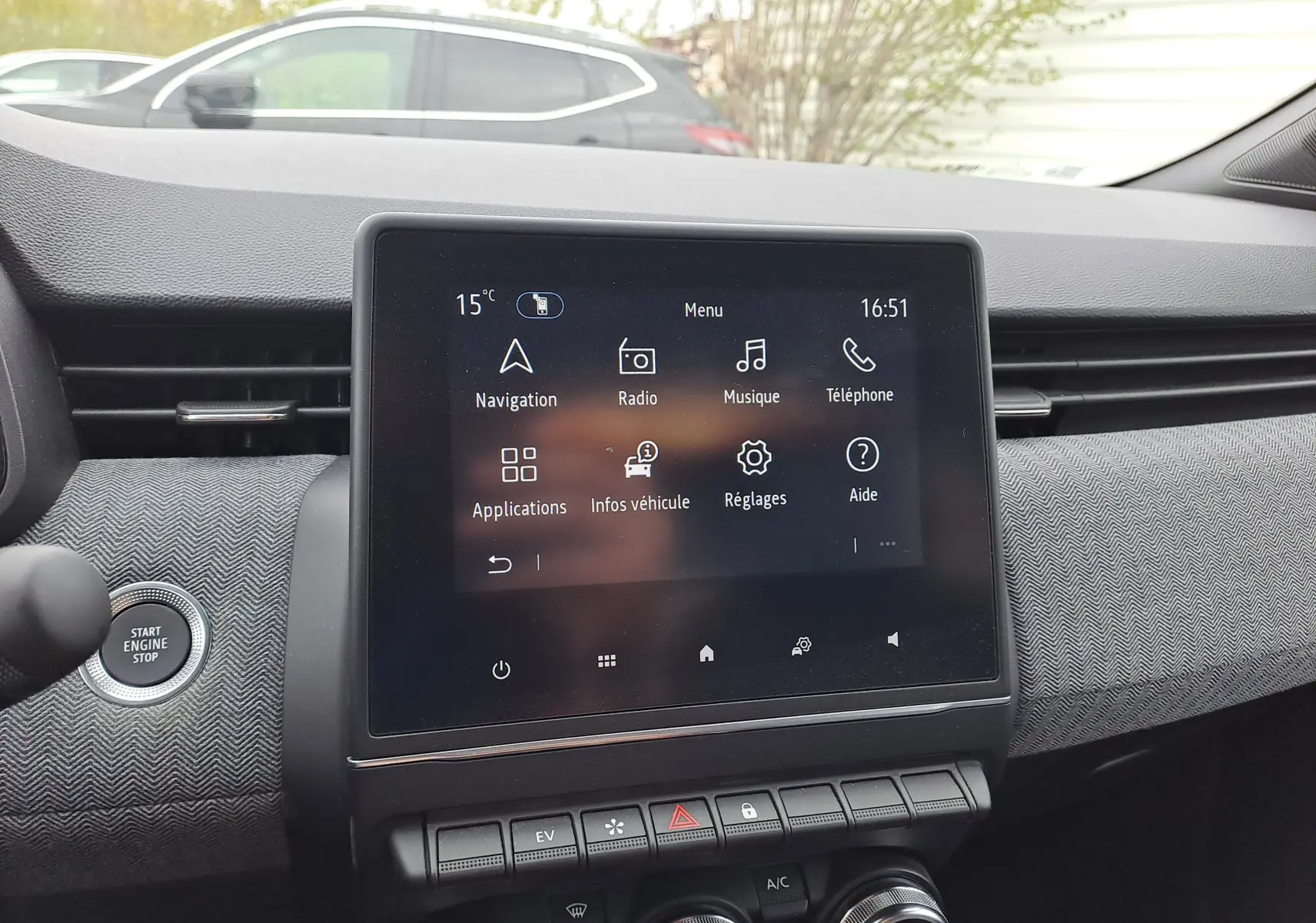 Vue intérieure centrée sur l’écran tactile du tableau de bord de la Renault Clio V hybride, avec bouton Start/Stop visible à gauche.