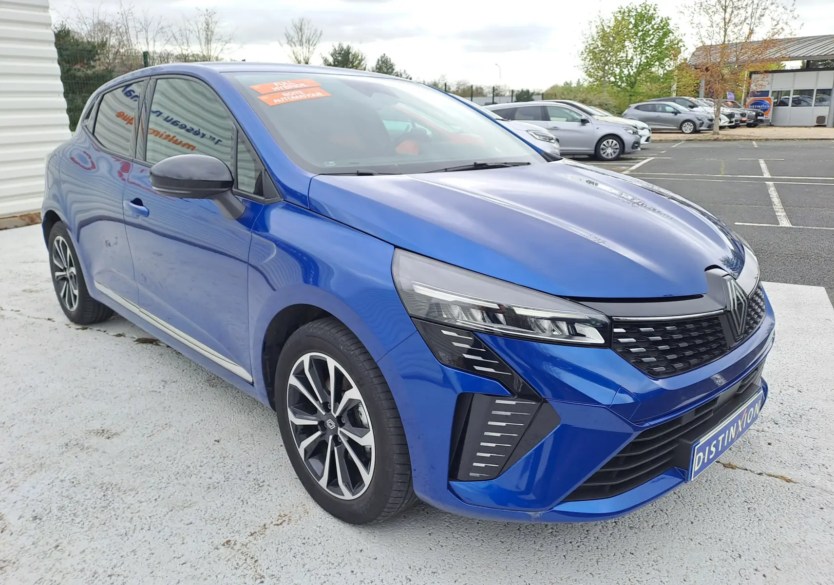 Renault Clio V bleu Iron Metal vue 3/4 avant droit, avec calandre noire et phares LED distinctifs.