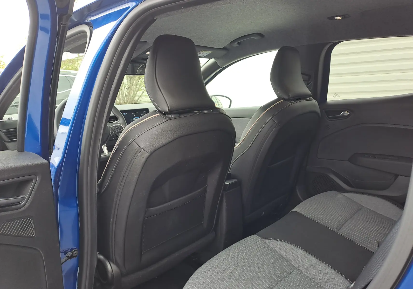 Vue intérieure arrière de la Renault Clio V bleu iron metal, montrant les sièges avant en cuir noir et la banquette arrière tissu gris.