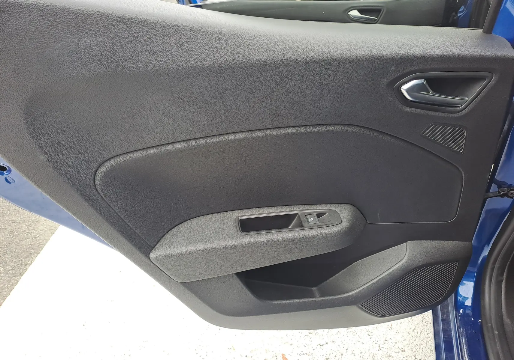 Vue rapprochée de la porte intérieure côté gauche d'une Renault Clio V bleu iron metal, avec poignée et commande de vitre.