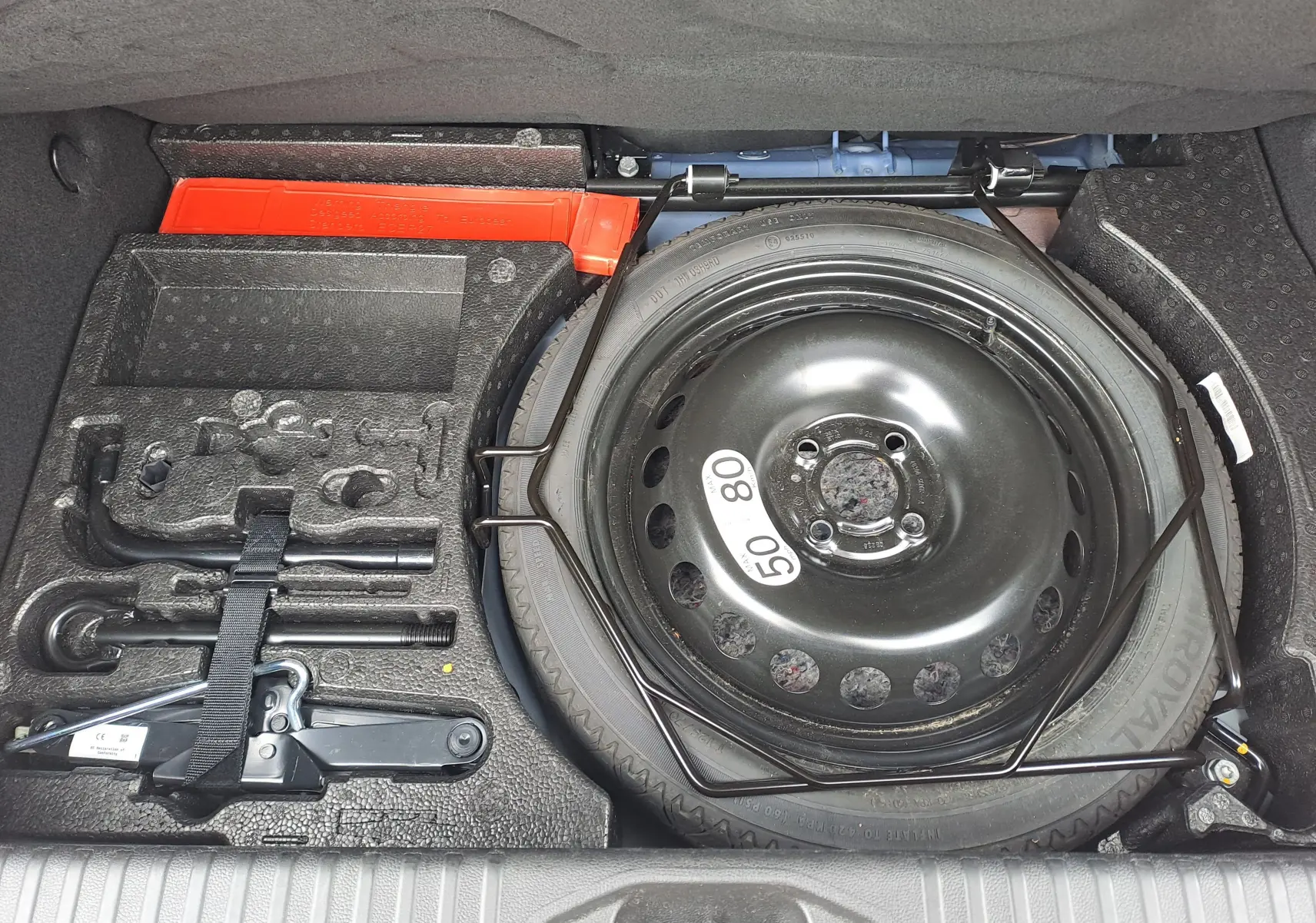 Vue du coffre de la Renault Clio V bleu iron metal, montrant la roue de secours et les outils de dépannage rangés.