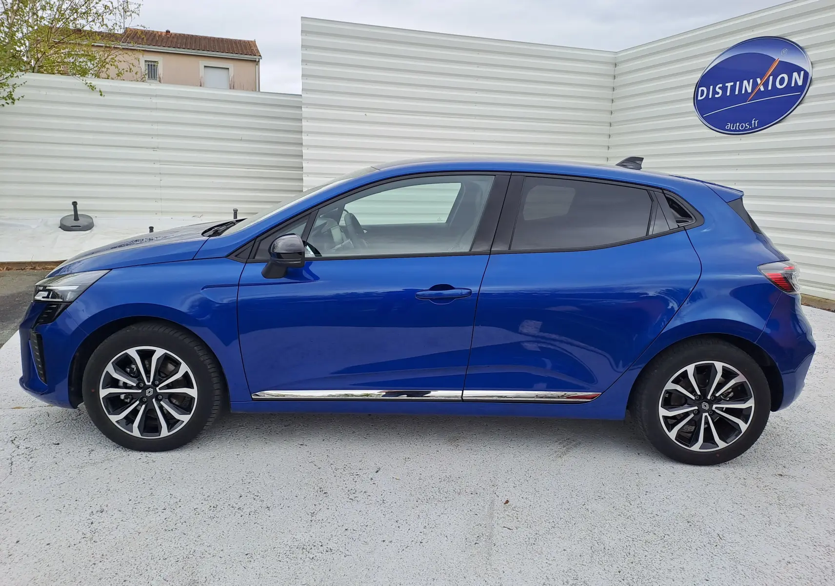 Profil droit de la Renault Clio V hybride bleu Iron Metal 2025 avec jantes alliage et détails chromés sur bas de caisse.