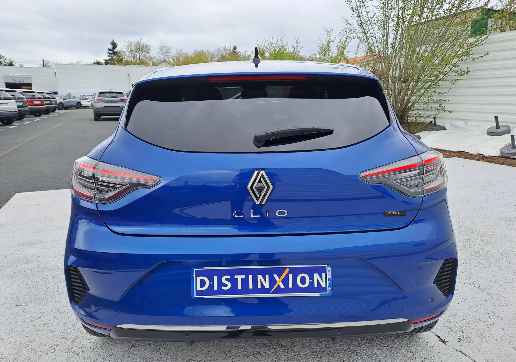 Vue arrière d'une Renault Clio V bleu iron metal avec feux LED et logo central, stationnée sur sol clair.