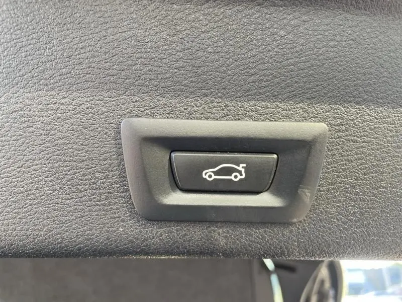 Bouton de déverrouillage électrique du coffre sur un BMW X4 30DA X DRIVE noir métal, vue en gros plan intérieur.
