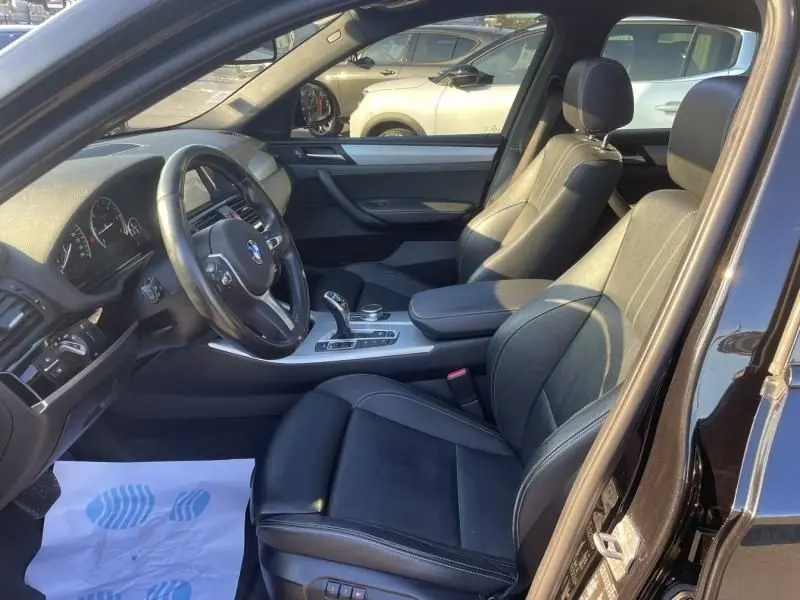 Vue intérieure côté conducteur de la BMW X4 30DA X DRIVE noire métal, sièges cuir noir et console centrale M Sport.