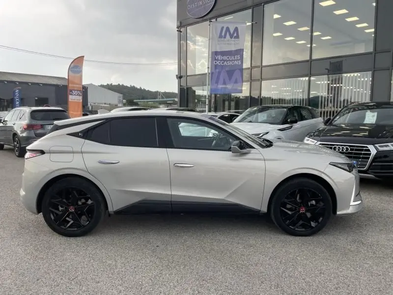 Vue de profil côté gauche d'une DS4 hybride rechargeable gris clair avec jantes noires, devant un concessionnaire.