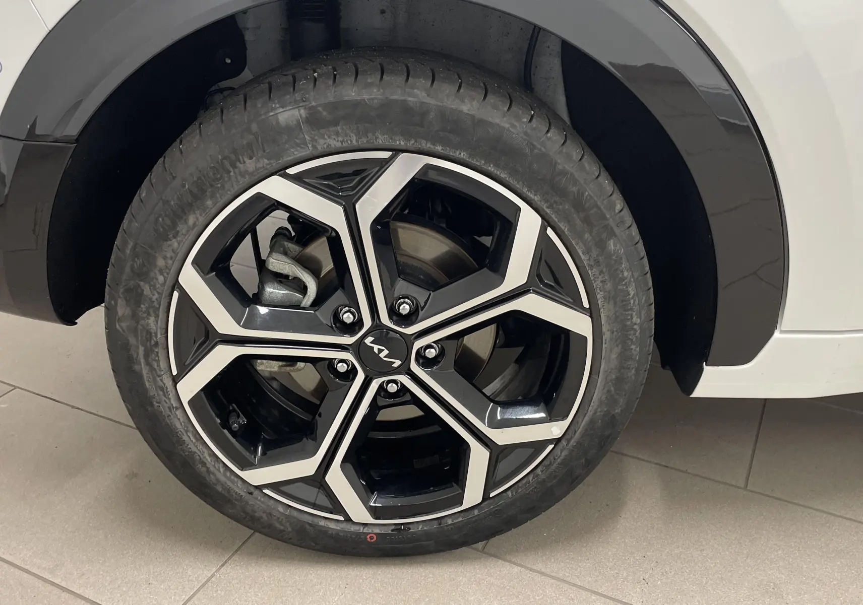 Gros plan sur la roue avant gauche du KIA NIRO blanc 2025, mettant en valeur la jante alliage bicolore au design géométrique.