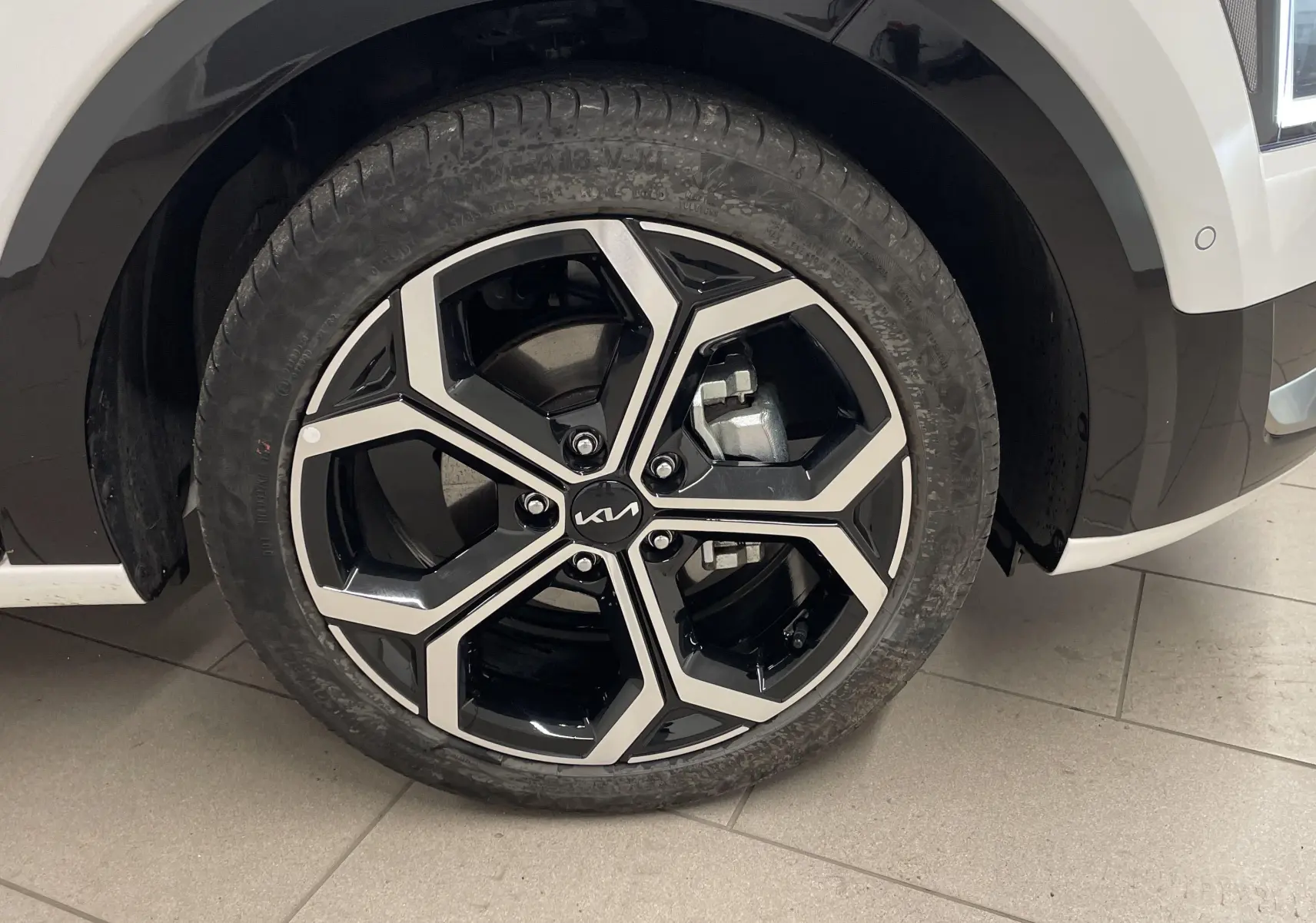 Gros plan sur la roue avant gauche du KIA NIRO blanc 2025, mettant en valeur la jante alliage noire et argentée au design moderne.