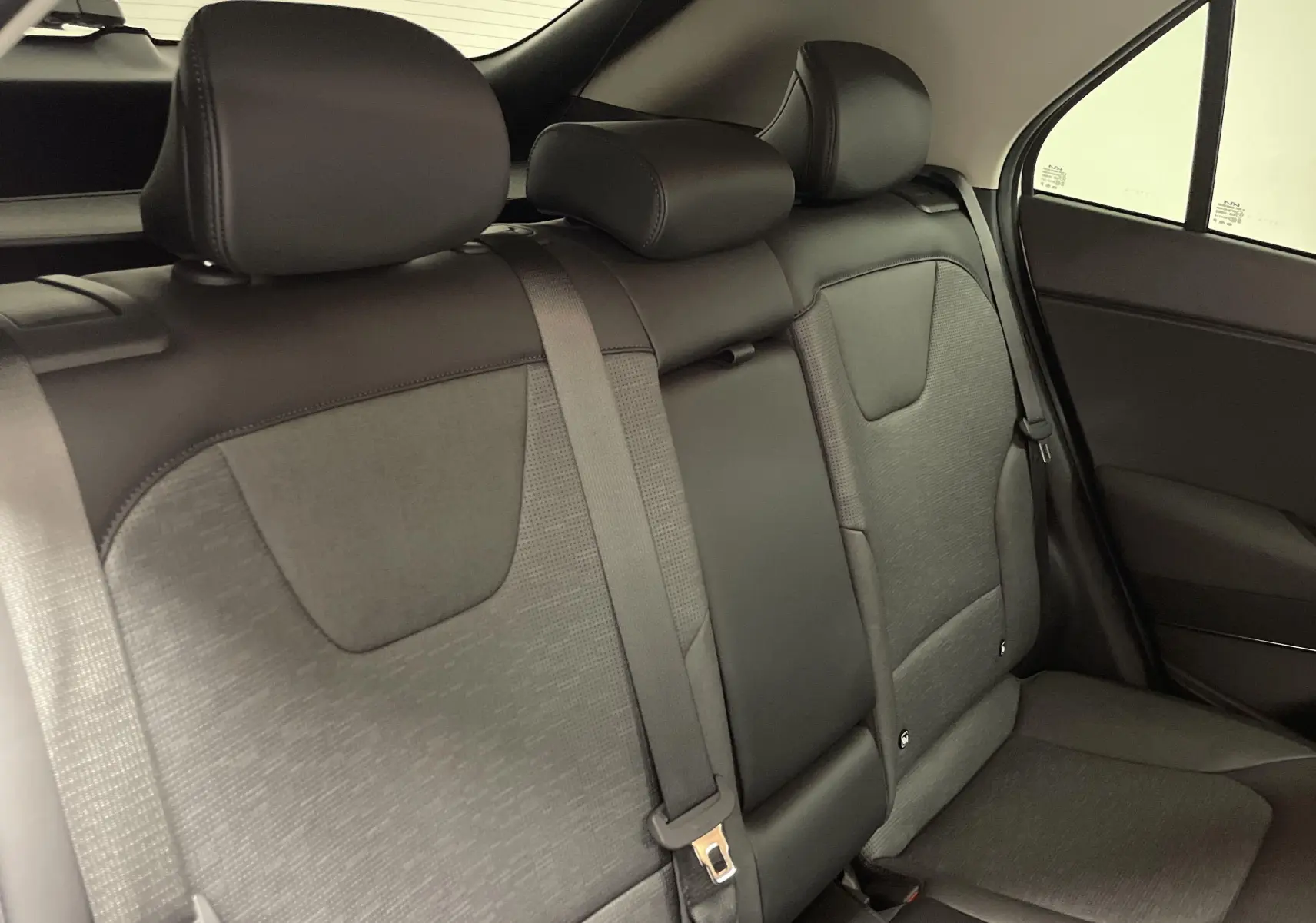 Vue intérieure du siège arrière droit du Kia Niro 2025, tissu gris et appuie-têtes noirs visibles.