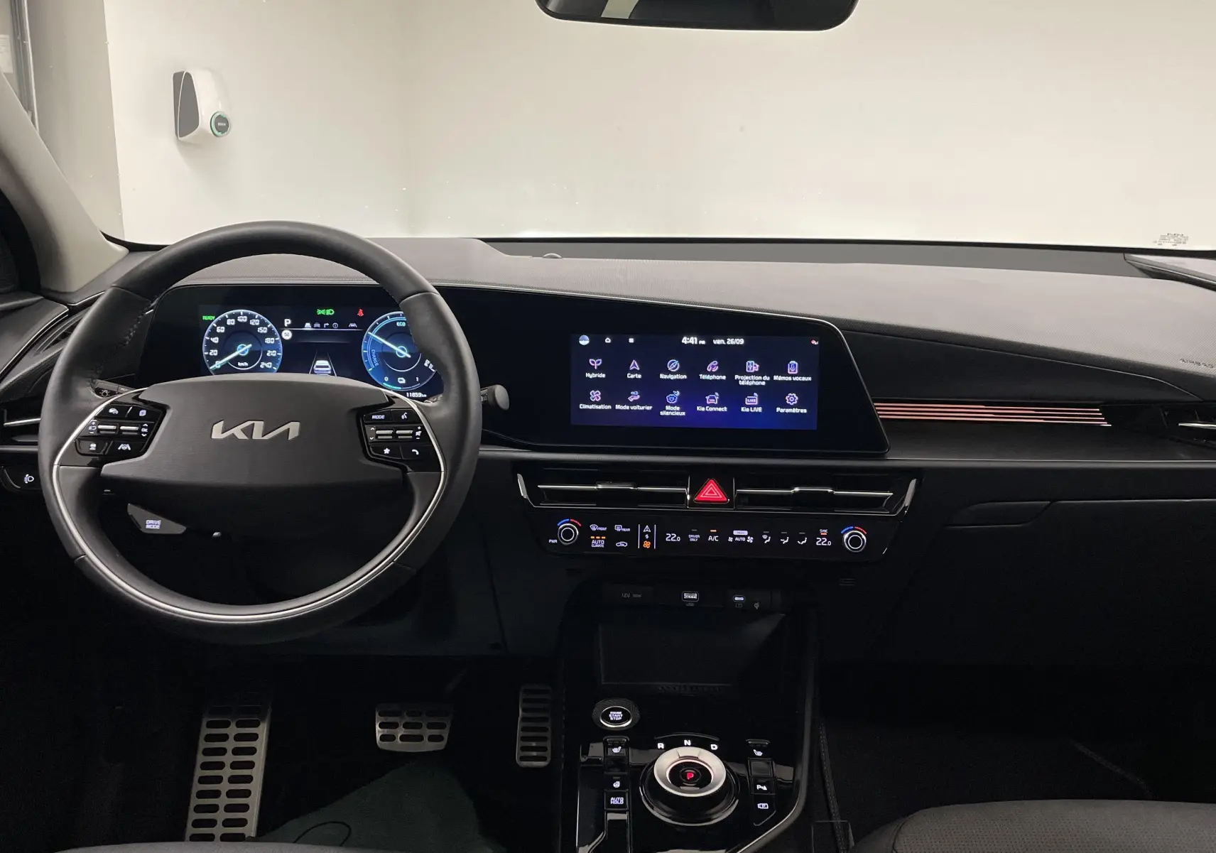 Vue intérieure du tableau de bord du Kia Niro 2025 blanc, avec écran tactile et volant multifonction.