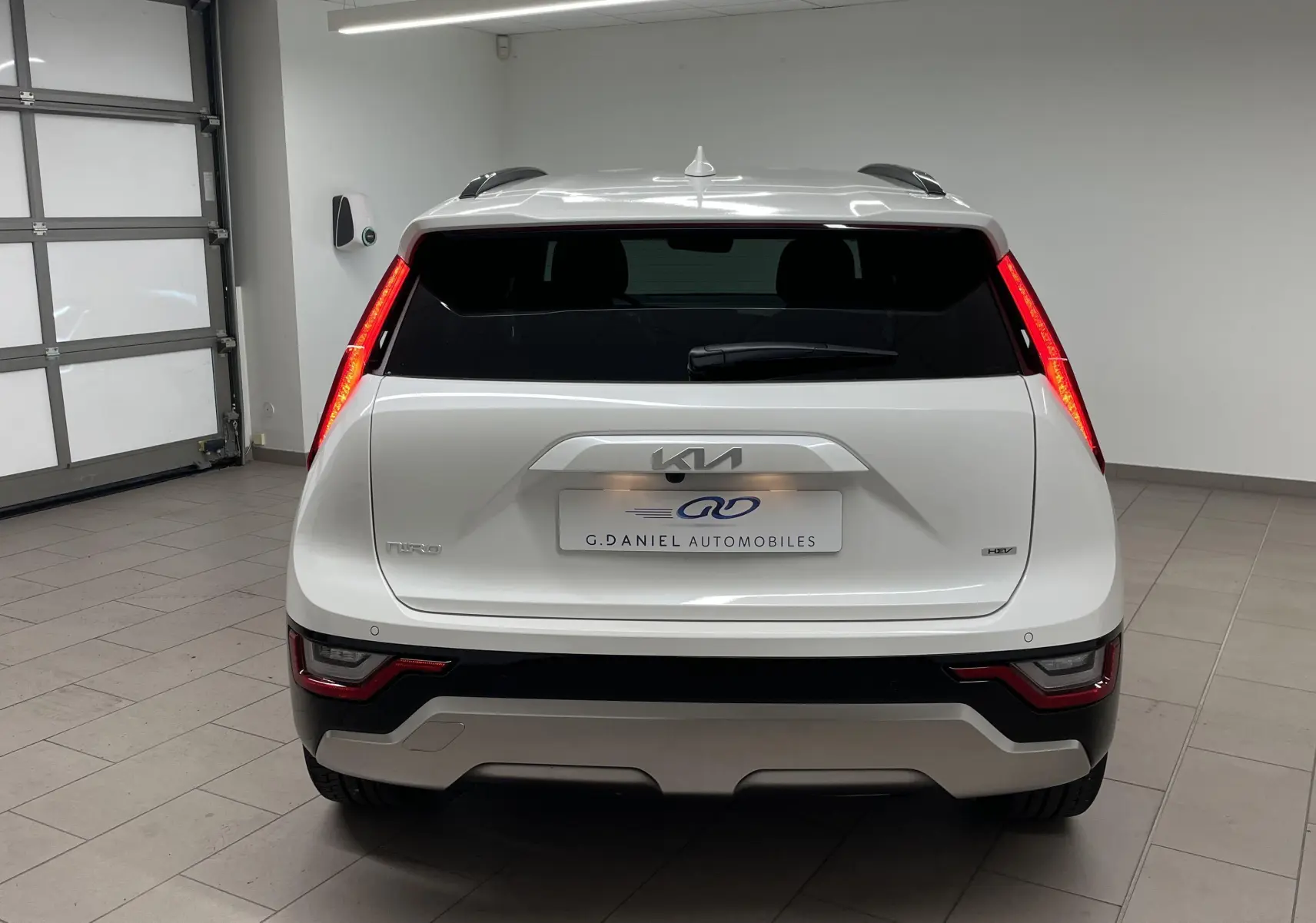 Vue arrière d'un Kia Niro blanc 2025 hybride essence, avec feux arrière verticaux allumés en intérieur showroom.