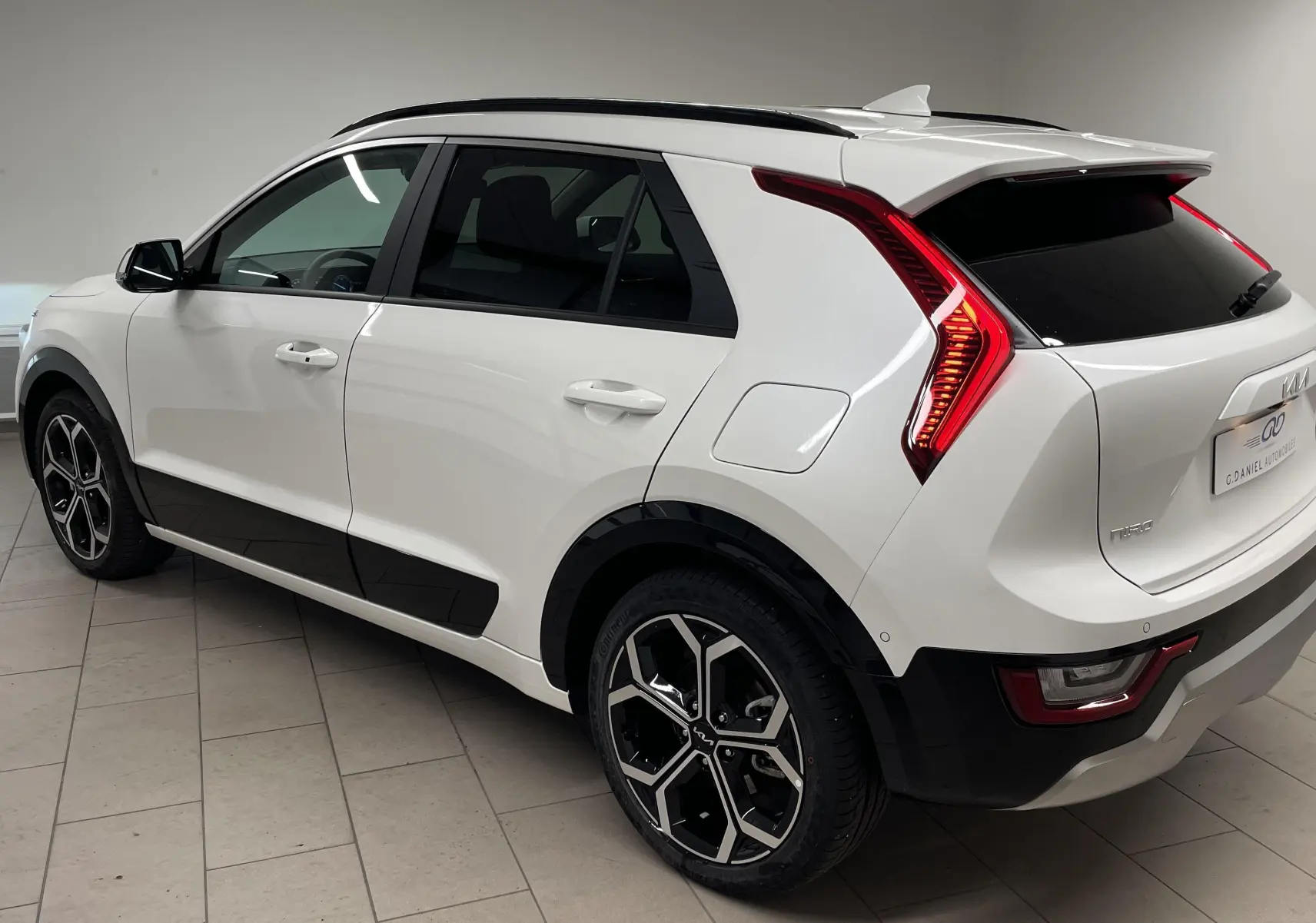 KIA NIRO blanc vue 3/4 arrière côté gauche, avec feux arrière LED en forme de boomerang et jantes noires stylisées.