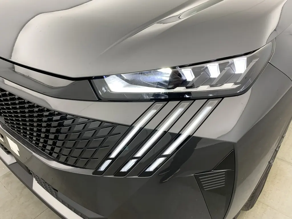 Gros plan sur le phare avant droit et la calandre noire laquée du Peugeot 3008 Hybrid gris Titane avec bandes LED distinctives.