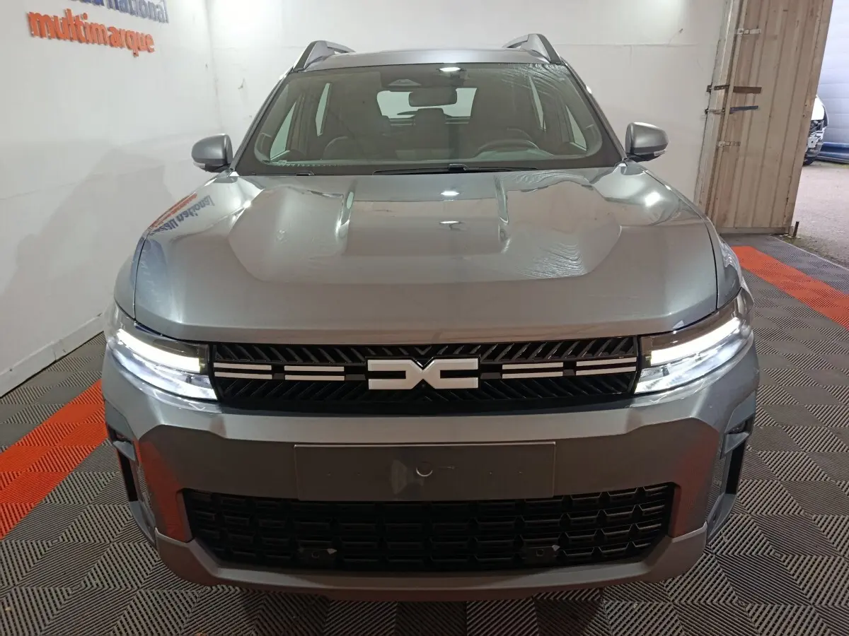 Vue avant du Dacia Bigster gris foncé avec calandre noire et feux LED allumés en intérieur.