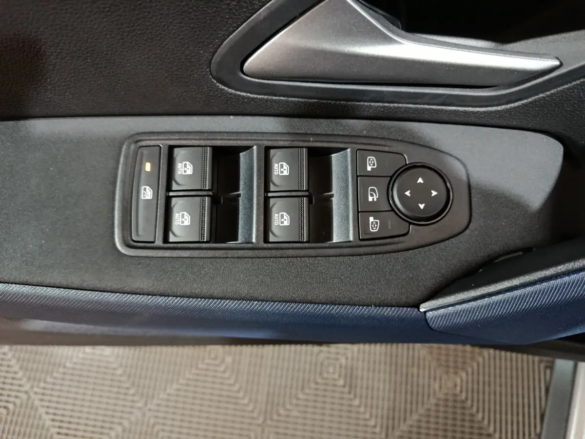 Gros plan sur les commandes des vitres électriques et des rétroviseurs sur la porte intérieure d'une Dacia Bigster gris foncé.