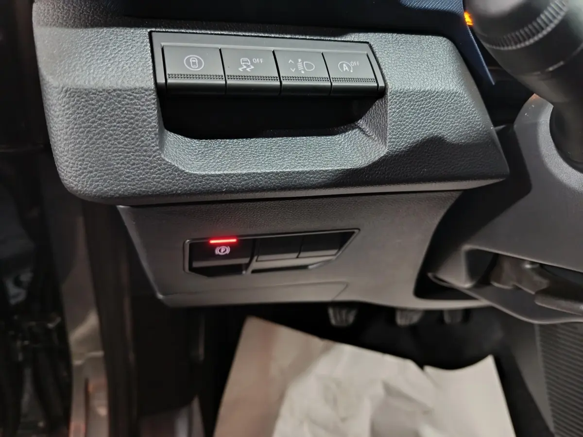Détail des commandes sous le tableau de bord côté gauche du Dacia Bigster gris foncé, avec bouton frein à main électrique allumé.