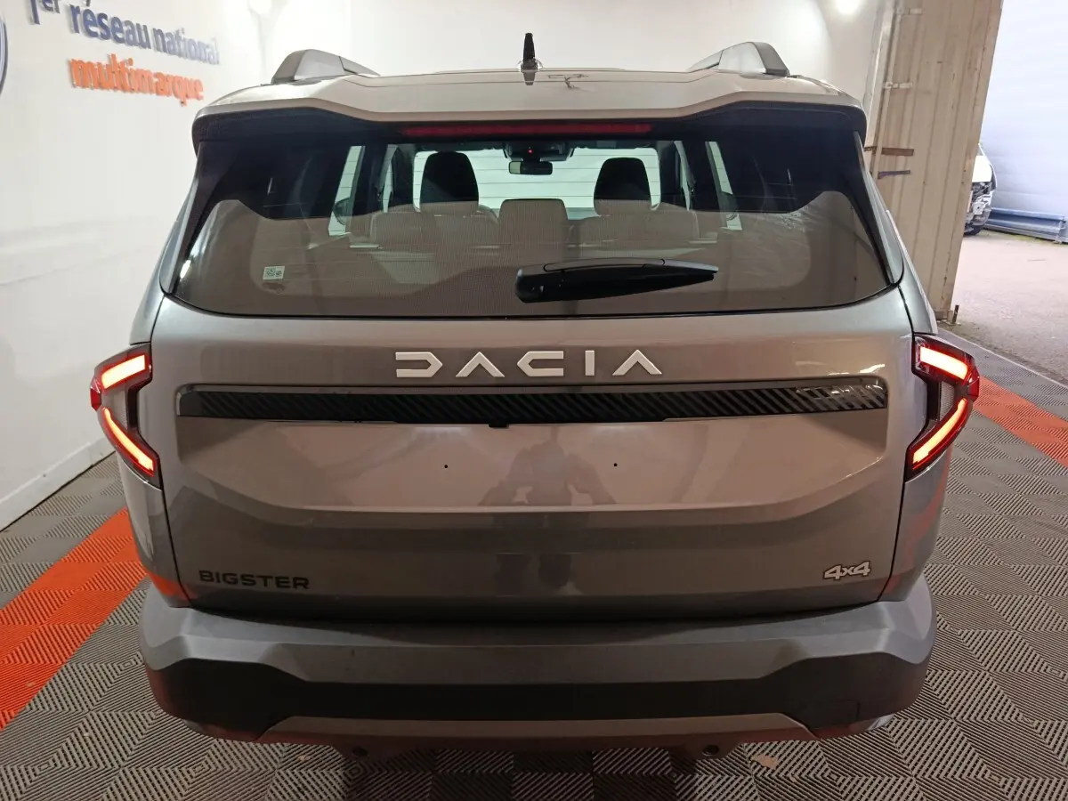 Vue arrière du Dacia Bigster gris foncé 4x4 avec feux LED allumés dans un garage intérieur.