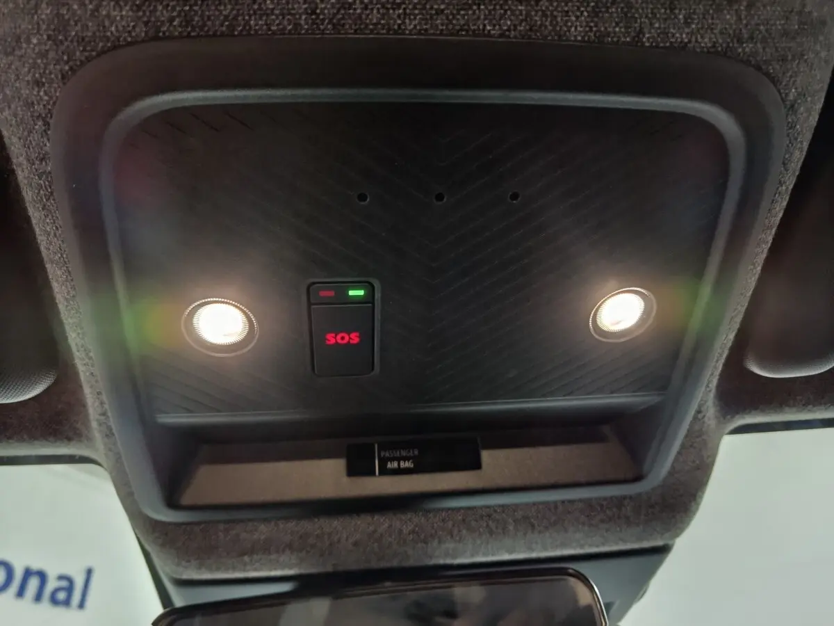 Vue intérieure en gros plan du plafonnier noir avec bouton SOS rouge et deux lampes allumées du Dacia Bigster gris foncé.