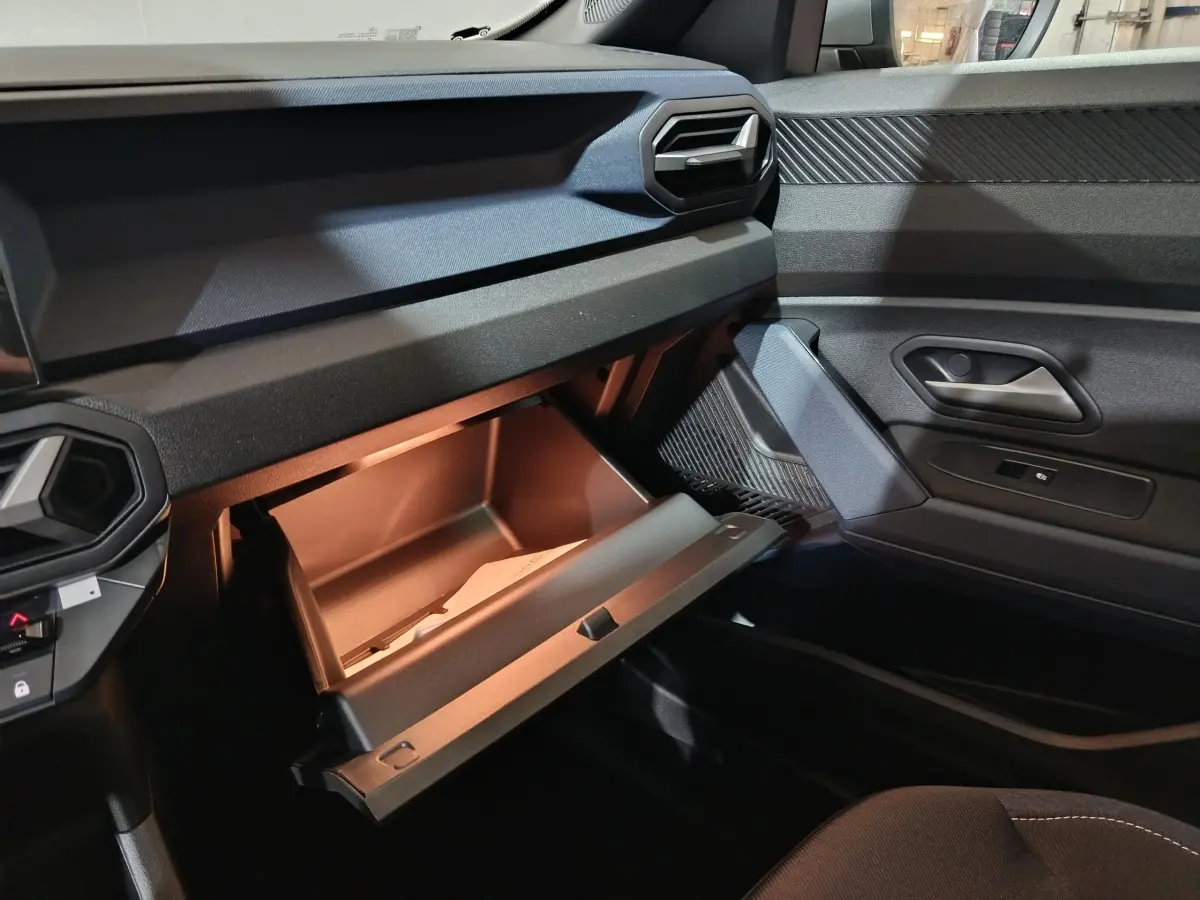 Vue intérieure côté passager du tableau de bord gris foncé du Dacia Bigster 2025 avec boîte à gants ouverte et porte de portière visible.