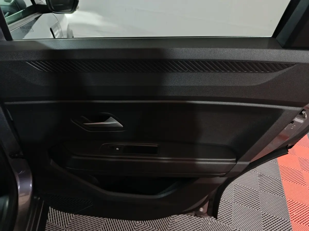 Vue intérieure côté gauche de la porte avant grise foncée du Dacia Bigster avec poignée et commande de vitre électrique.