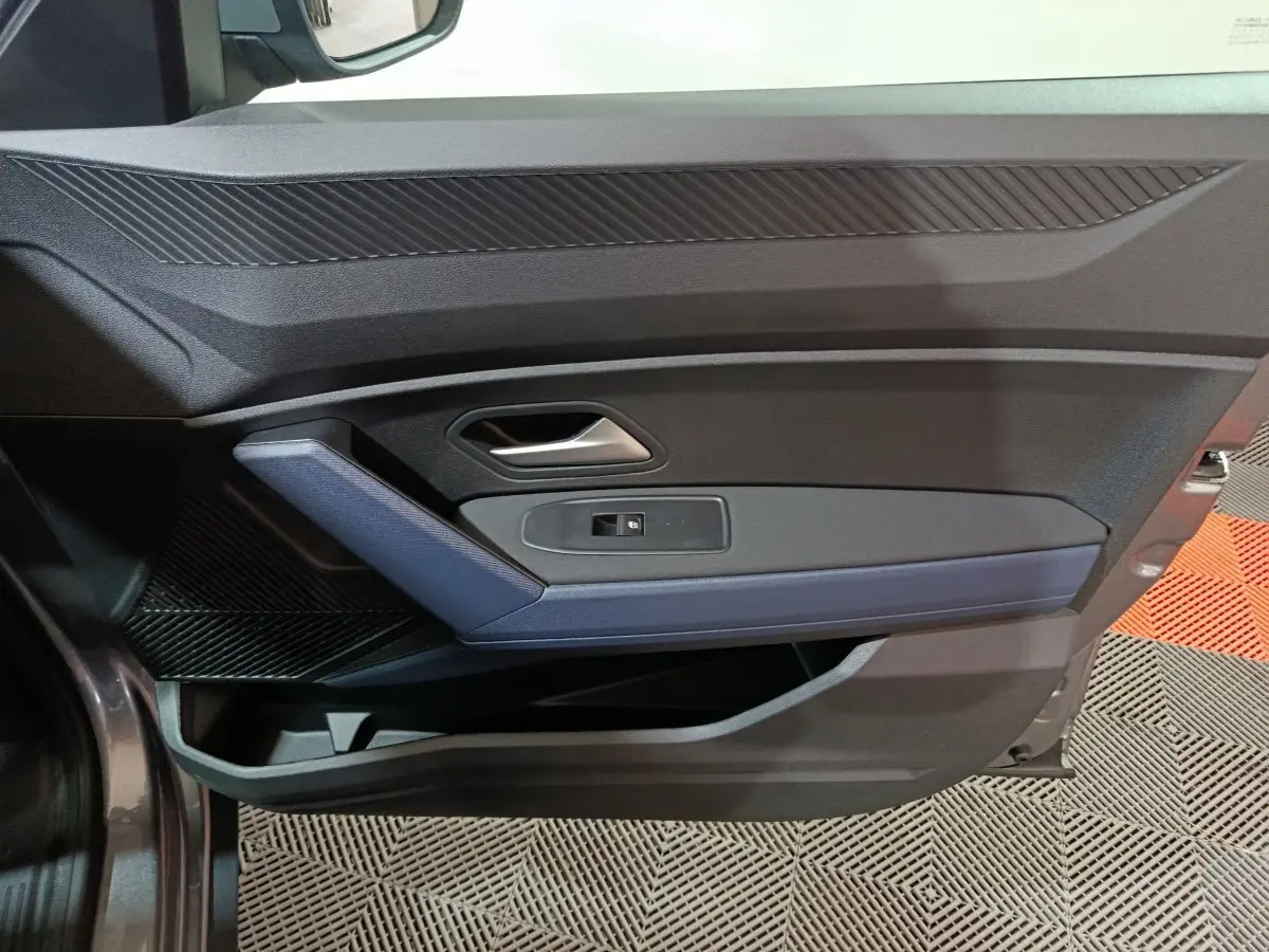Vue intérieure de la porte avant gauche gris foncé du Dacia Bigster avec poignée argentée et insert bleu.
