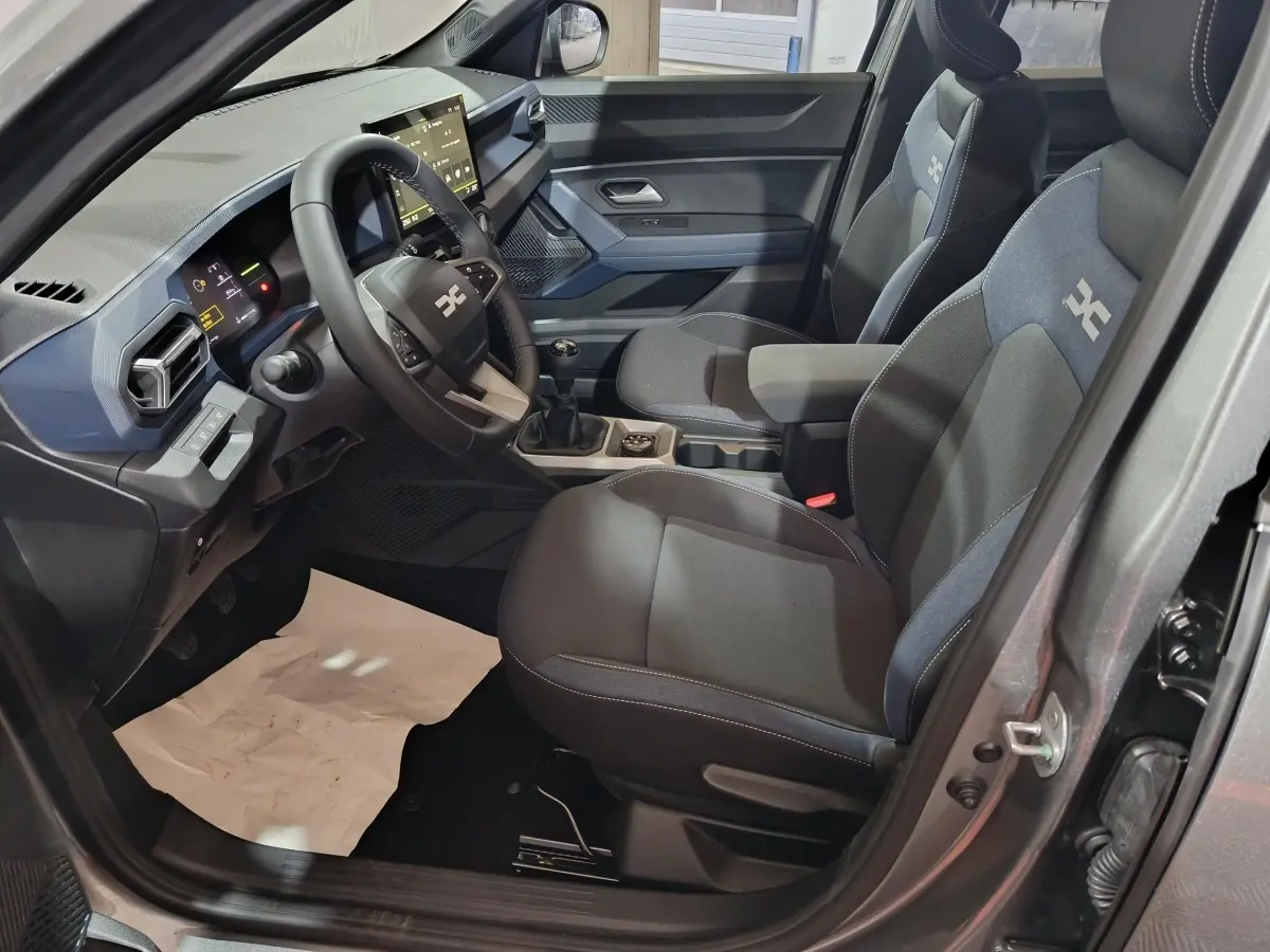 Vue intérieure côté conducteur du Dacia Bigster gris foncé 2025, montrant sièges et tableau de bord avec écran tactile.