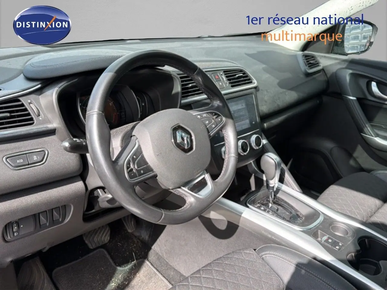 Vue intérieure du poste de conduite du Renault Kadjar gris Highland, avec volant multifonction et console centrale à boîte automatique.