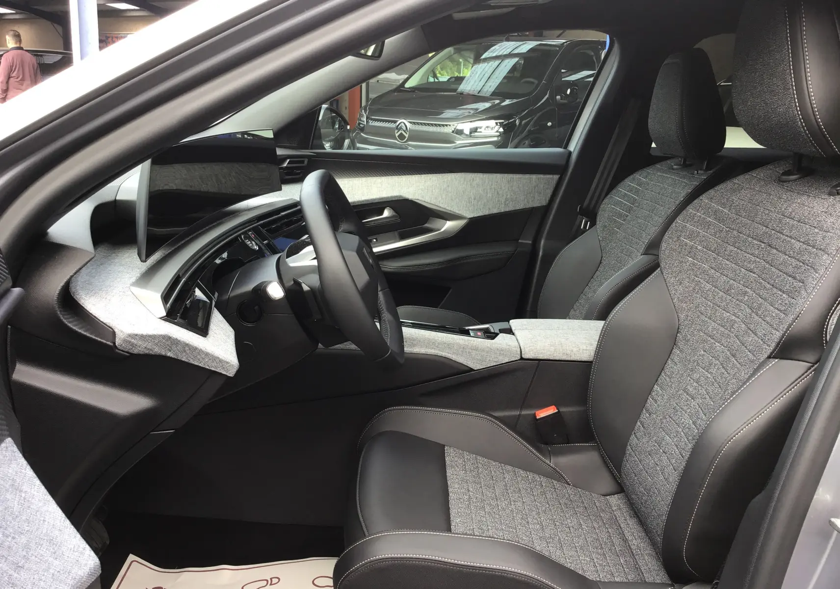 Vue intérieure côté conducteur du Peugeot 3008 1.2 Hybrid 145 Allure, sièges tissu gris et cuir noir, tableau de bord moderne.