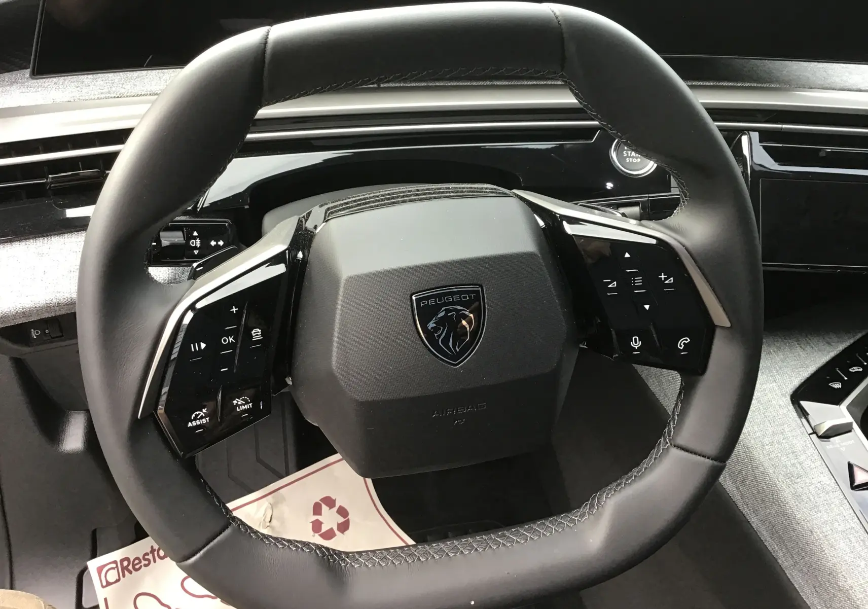 Vue rapprochée du volant cuir noir du Peugeot 3008 1.2 Hybrid 145 Allure avec commandes intégrées et tableau de bord gris.