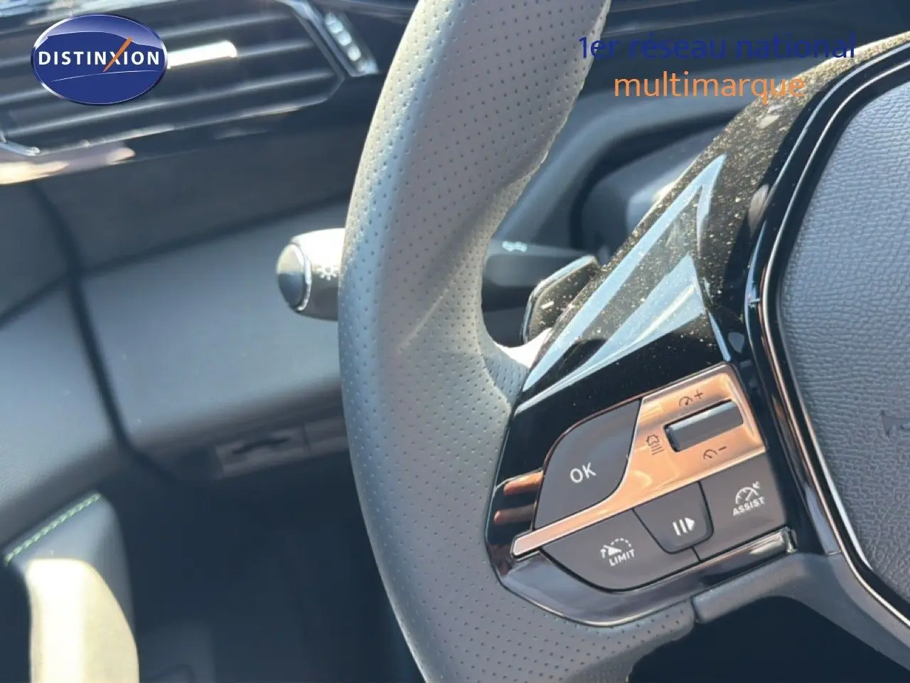 Gros plan sur le volant perforé gris clair de la Peugeot 308 Hybrid 145ch GT avec commandes intégrées et finition noire brillante.