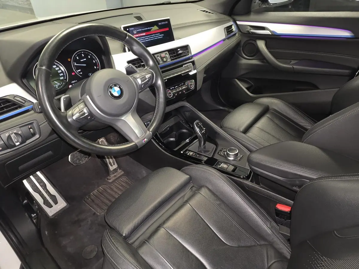 Intérieur noir cuir du BMW X2 M Sport 2023, vue côté conducteur avec volant M et éclairage d'ambiance violet.