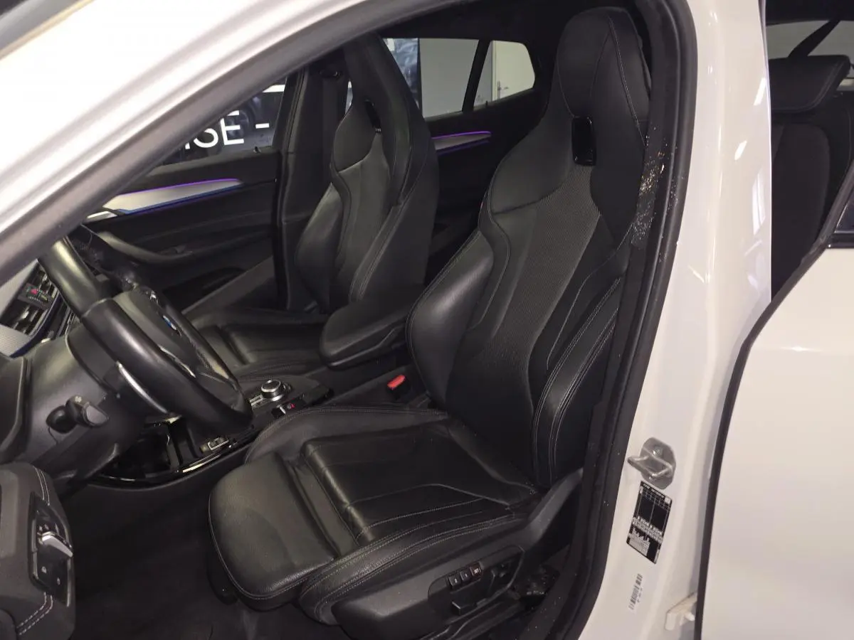 Vue intérieure côté gauche d'une BMW X2 blanche 2023 avec sièges sport M en cuir noir et éclairage d'ambiance violet.