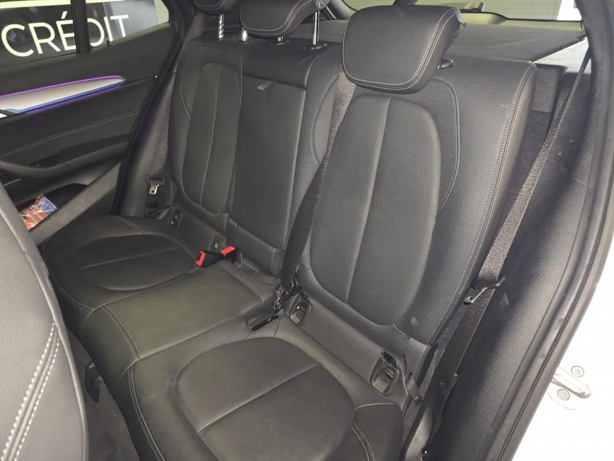 Vue intérieure arrière droite montrant la banquette en cuir noir perforé du BMW X2 sDrive18d M Sport blanc.