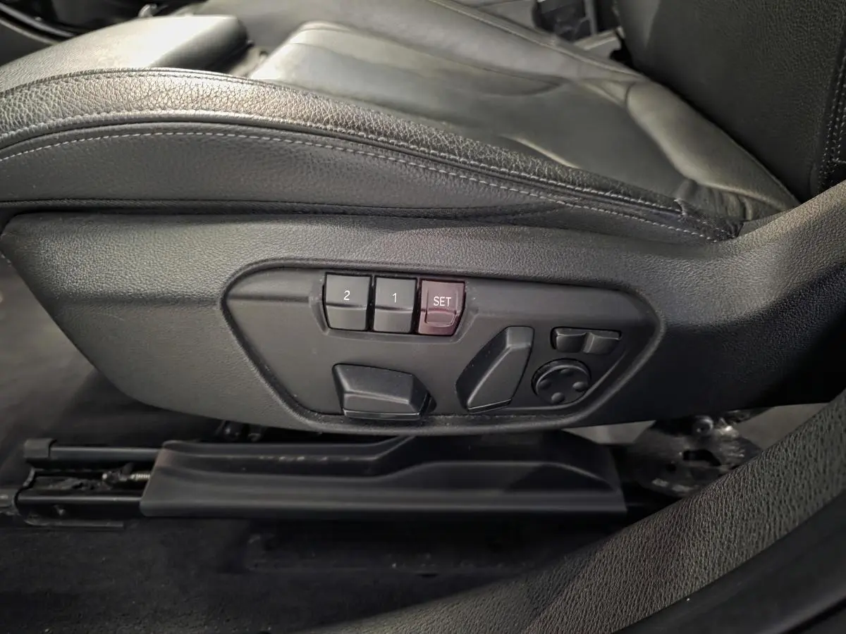 Détail des commandes de réglage électrique du siège conducteur en cuir noir dans une BMW X2 M Sport blanche.