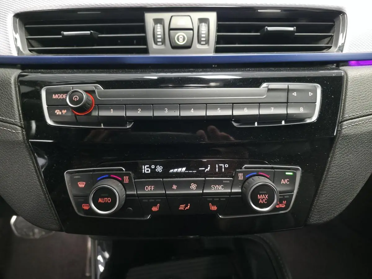 Panneau de commande central noir brillant avec climatisation bi-zone et réglages multifonctions dans BMW X2 blanc 2023.