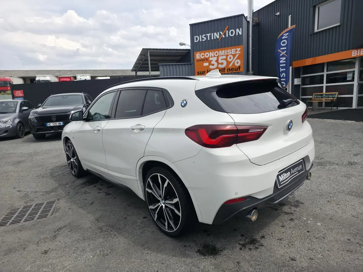 BMW X2 sDrive 18d blanc vue 3/4 arrière droit, jantes alliage 20'' style M Sport et double sortie d’échappement chromée.
