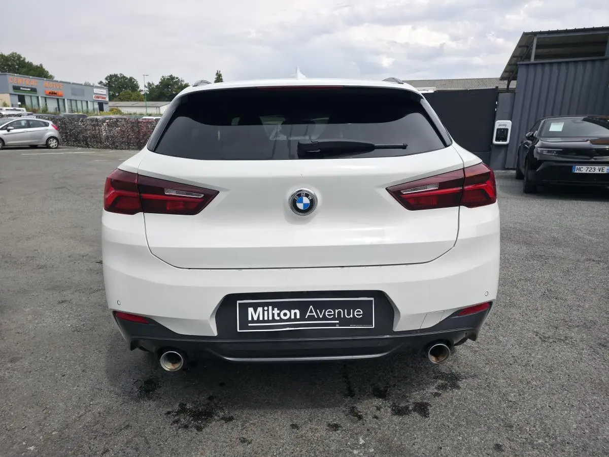 Vue arrière d'une BMW X2 sDrive 18d blanche avec double sortie d'échappement et feux arrière LED rouges.