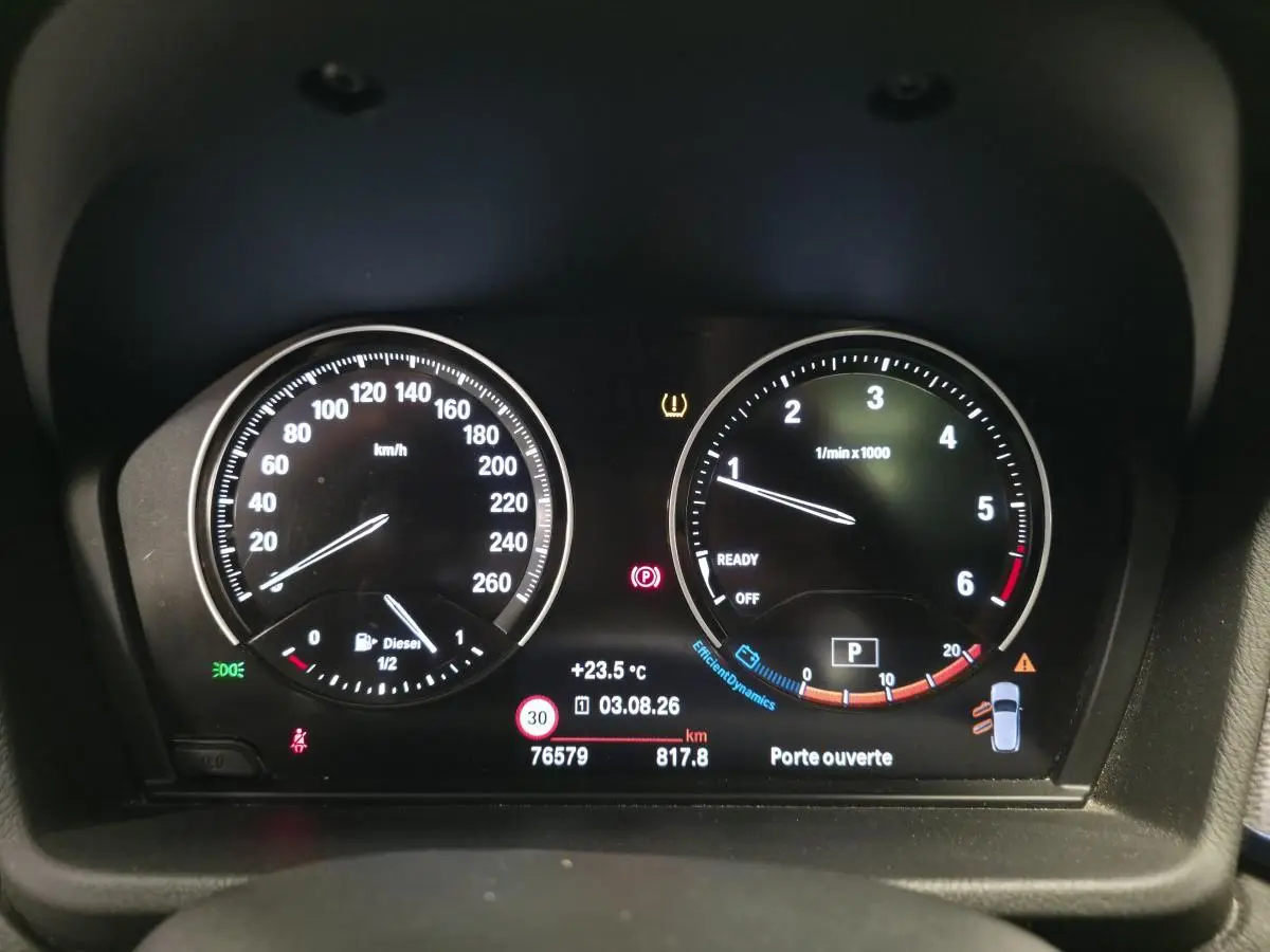 Tableau de bord numérique BMW X2 sDrive 18d 2023 affichant vitesse, régime moteur et alertes, vue frontale intérieure.