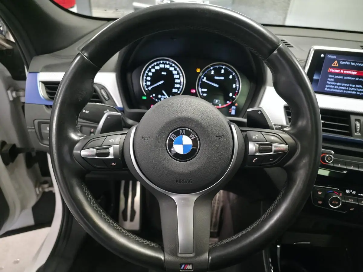 Vue rapprochée du volant cuir M noir avec commandes multifonctions et tableau de bord digital du BMW X2 blanc 2023.