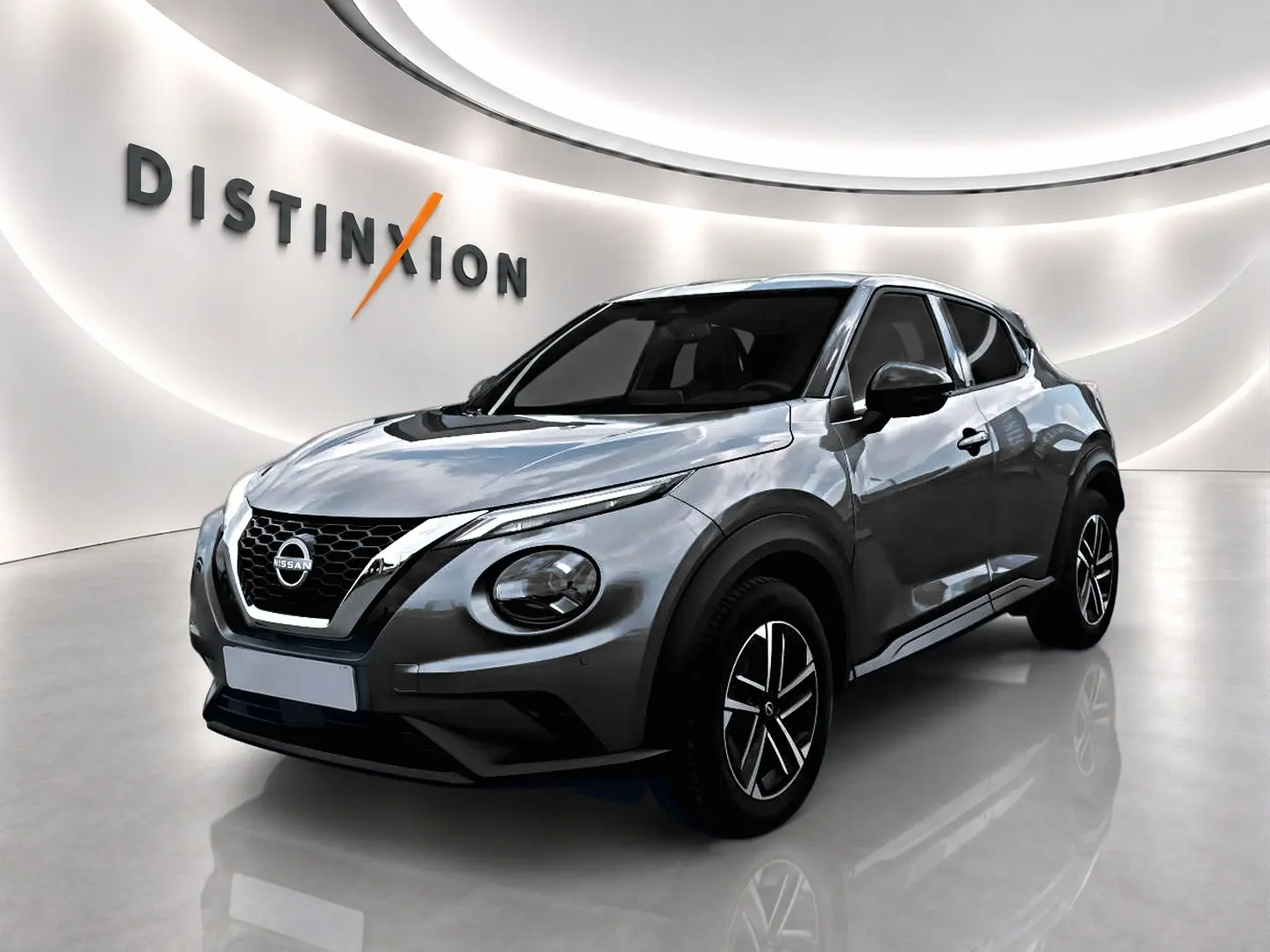 Nissan Juke gris 3/4 avant droit en showroom avec jantes alu et calandre chromée distinctive.