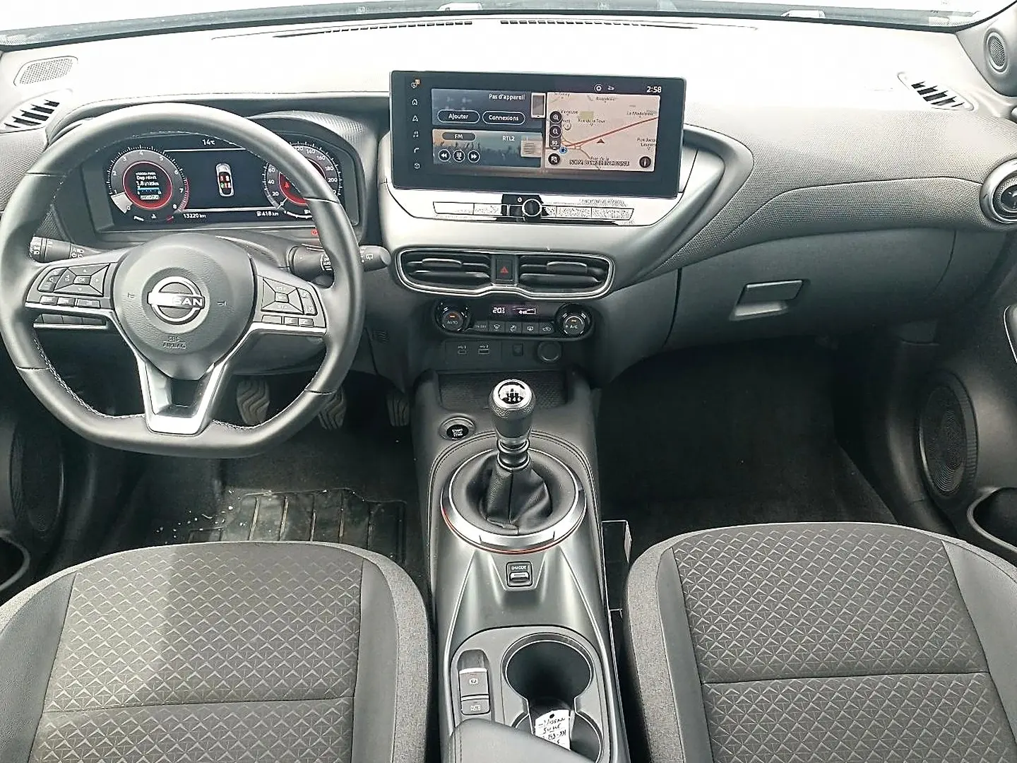 Vue intérieure avant du Nissan Juke 2025, tableau de bord et volant multifonction avec levier de vitesse manuel.