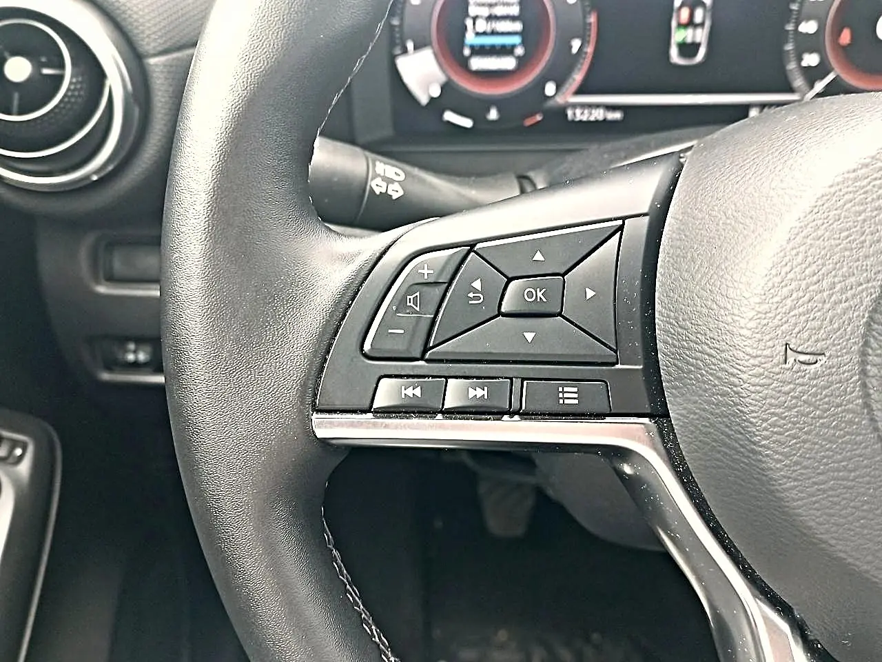 Gros plan sur le volant cuir noir multifonction côté gauche du Nissan Juke gris, avec commandes audio et navigation.