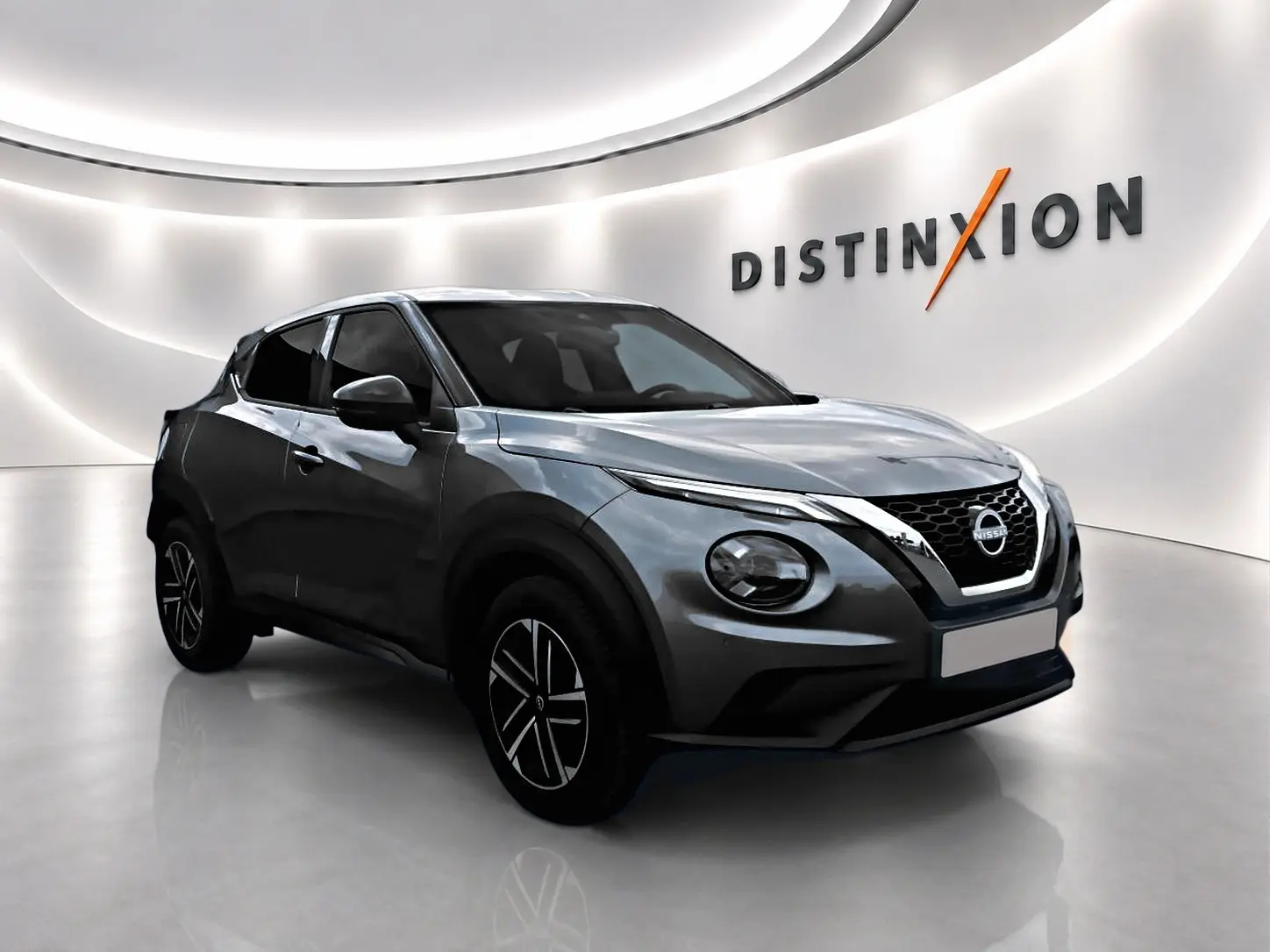 Nissan Juke gris en 3/4 avant droit dans un showroom lumineux avec jantes alliage et calandre chromée.