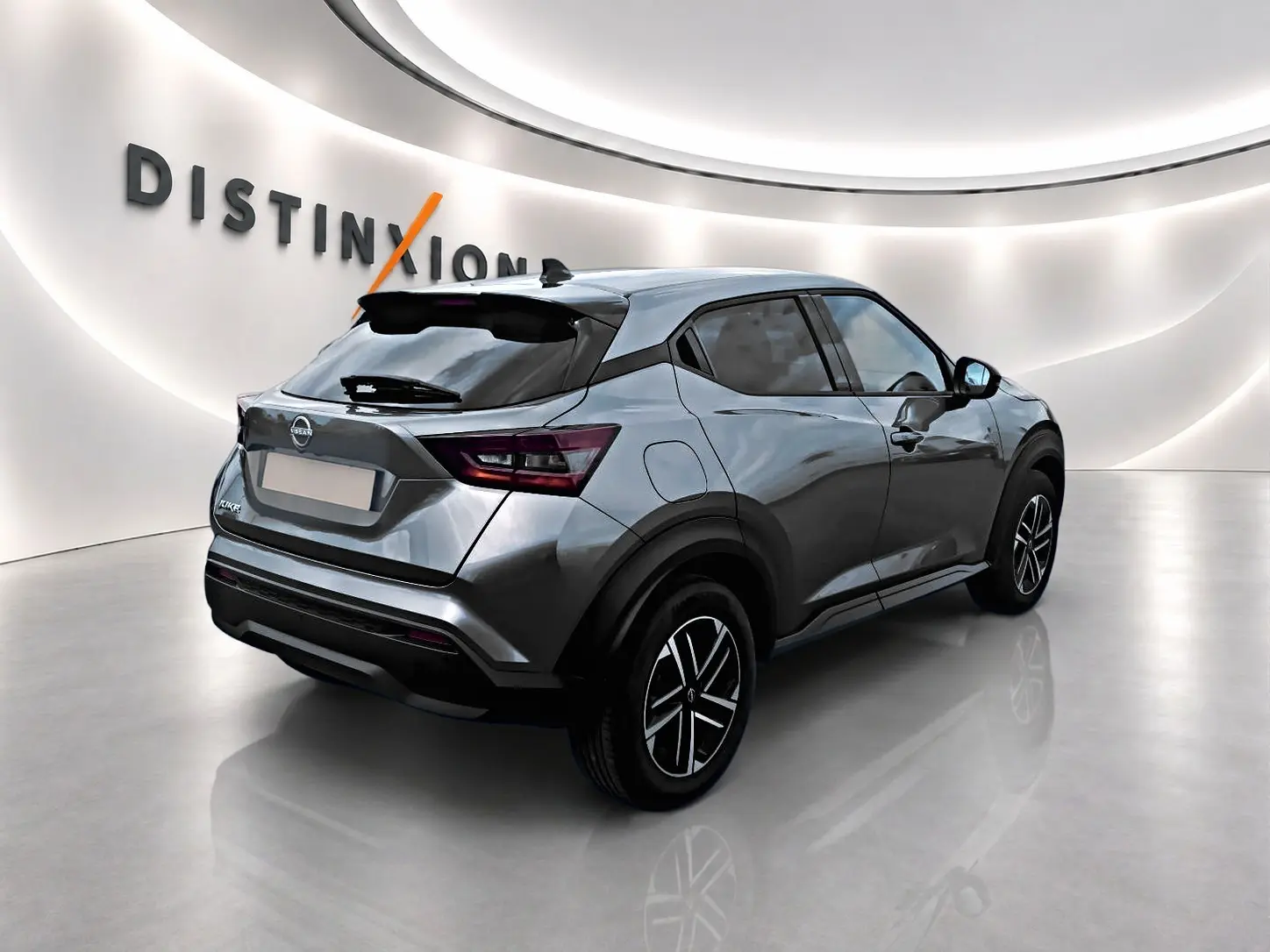 Vue 3/4 arrière droite du Nissan Juke gris 2025 avec jantes alliage et toit noir contrasté dans un showroom.