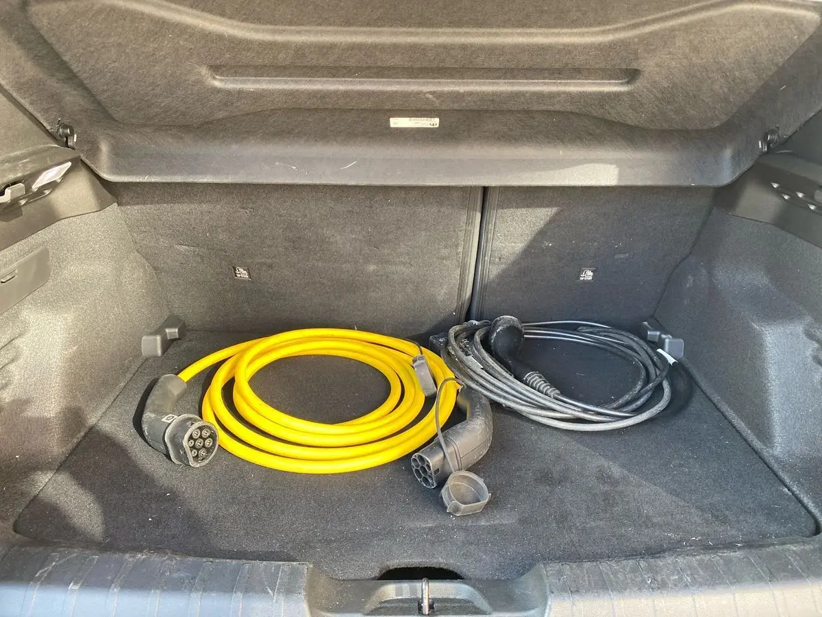 Coffre ouvert d'un Jeep Avenger électrique noir 2023, avec câbles de recharge jaune et noir rangés à l'intérieur.