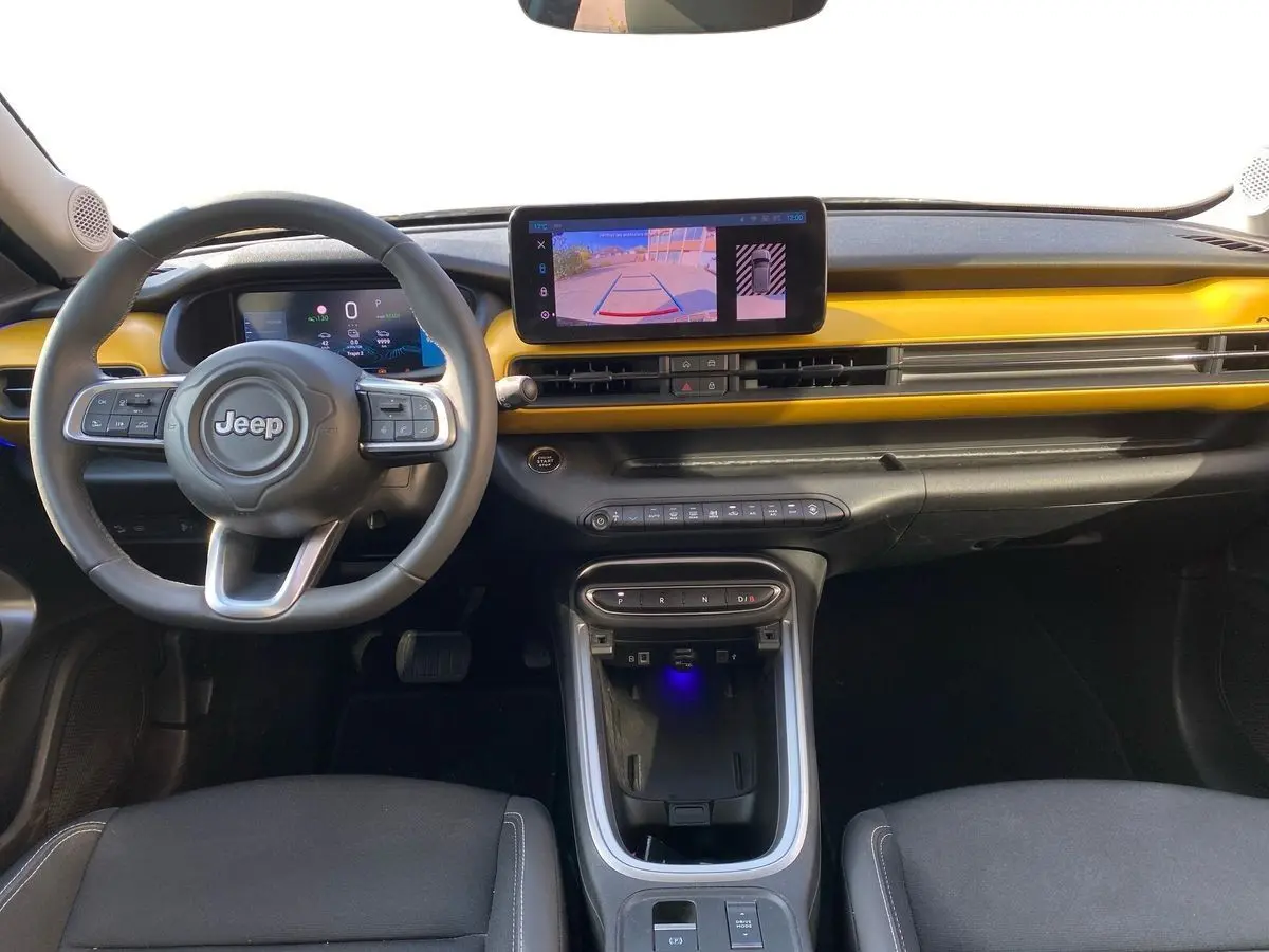 Intérieur du Jeep Avenger électrique 2023 vu de face, tableau de bord noir avec bande jaune et écran tactile central.