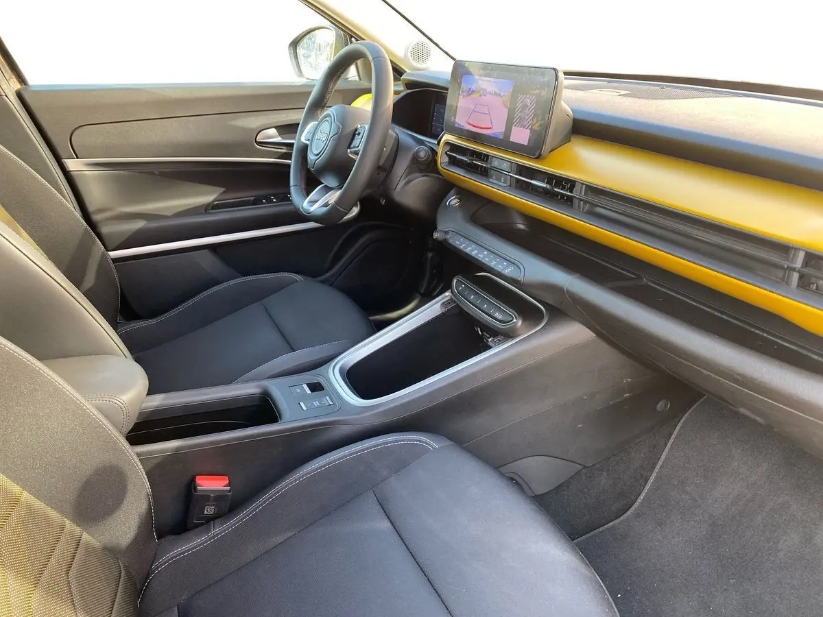 Vue intérieure côté conducteur du Jeep Avenger électrique 2023, tableau de bord noir et jaune avec écran tactile central.