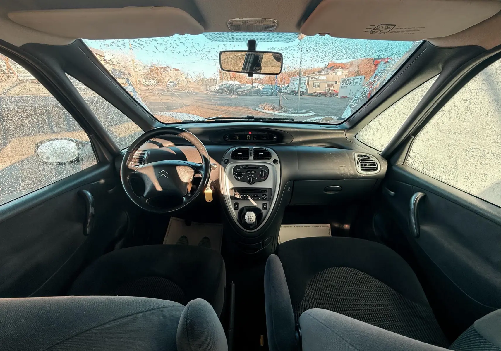 Vue intérieure avant du Citroën Xsara Picasso 2009, tableau de bord noir avec volant cuir et levier de vitesse manuel.