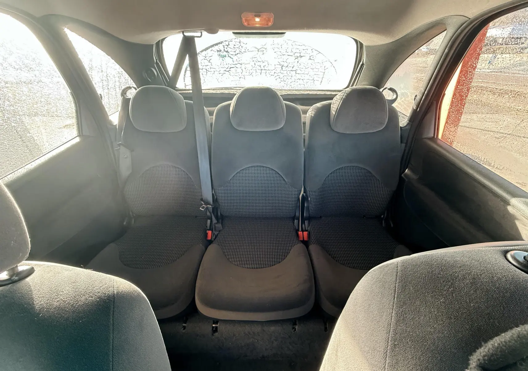 Vue intérieure arrière montrant les trois sièges arrière en tissu noir d'une Citroën Xsara Picasso beige.