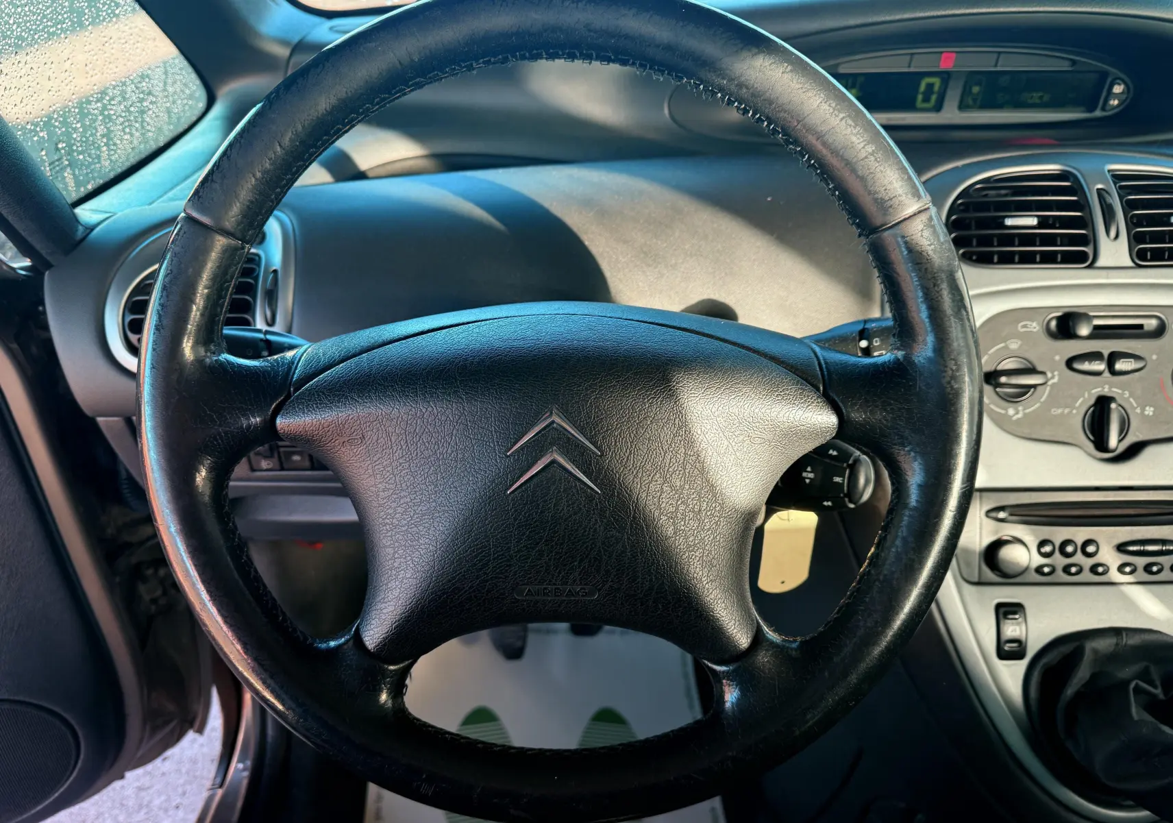 Vue rapprochée du volant en cuir noir d’une Citroën Xsara Picasso 2009, avec tableau de bord et commandes visibles.